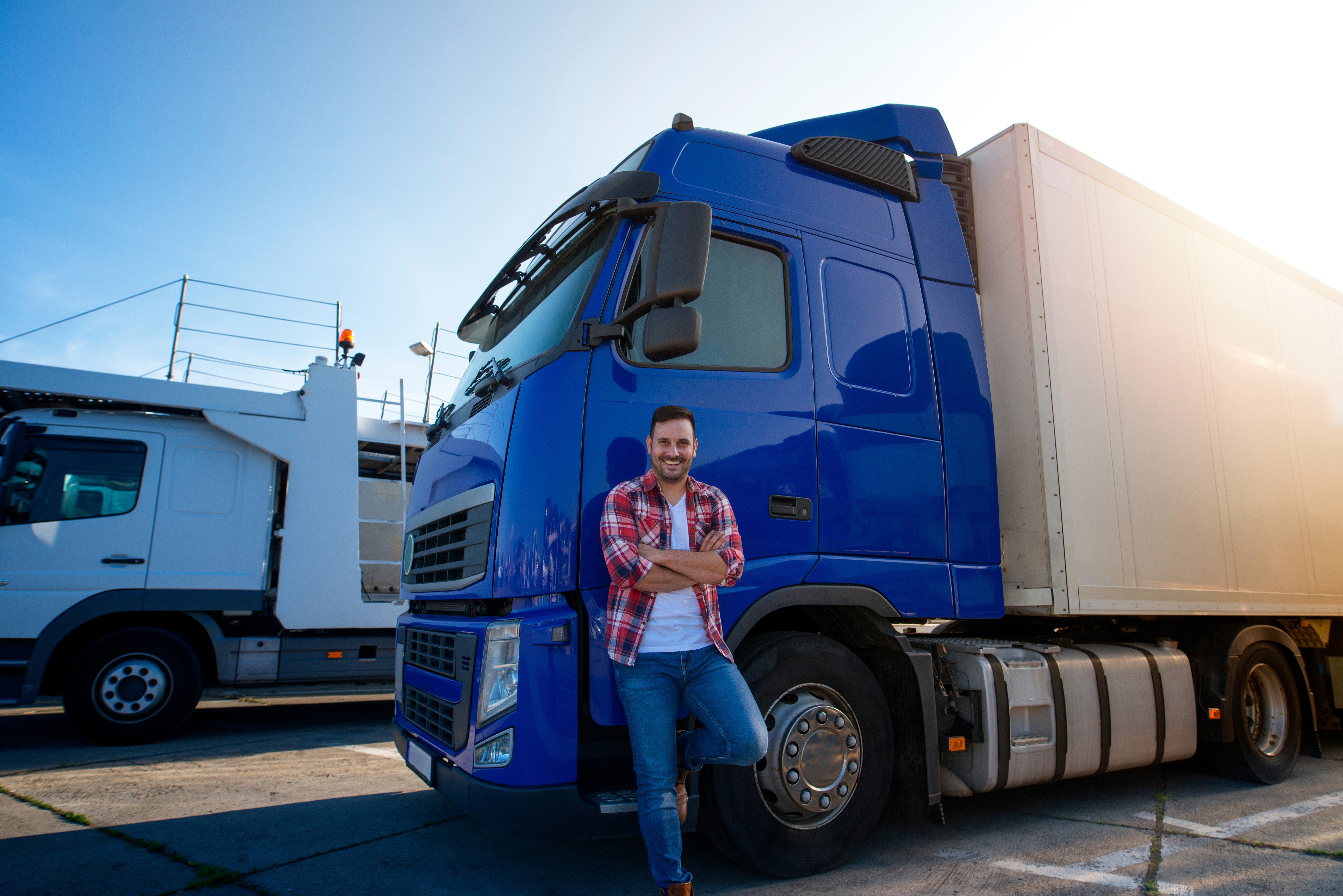 Person standing with arms crossed beside a blue semi‑truck and white trailer in a parking lot with another truck in the backgroundProvide your feedback on BizChat