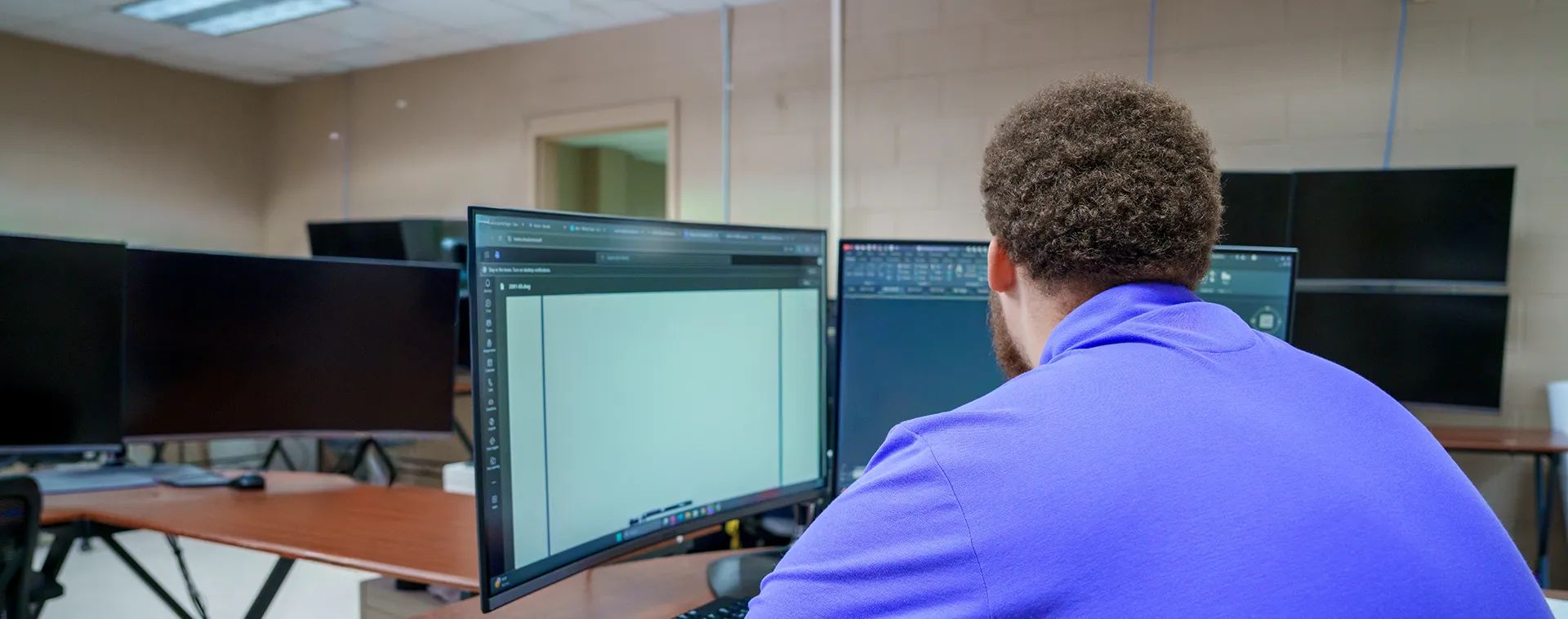 Student works at dual monitors displaying design software in a computer-aided design classroom.