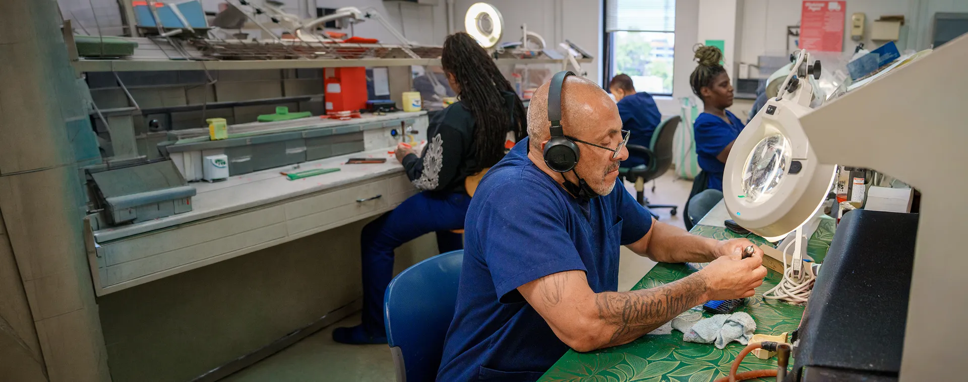 Students work at dental laboratory benches with magnifying lamps and dental model tools.
