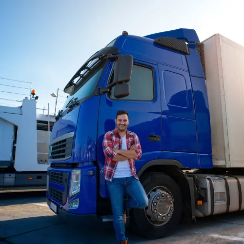 Person standing with arms crossed beside a blue semi‑truck and white trailer in a parking lot with another truck in the backgroundProvide your feedback on BizChat