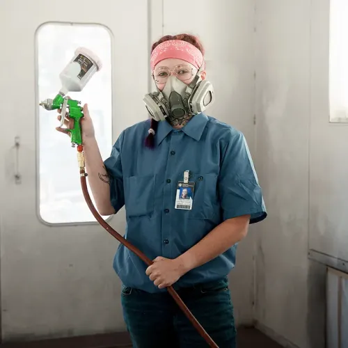 Student wearing a respirator holds a paint spray gun in an automotive paint booth.