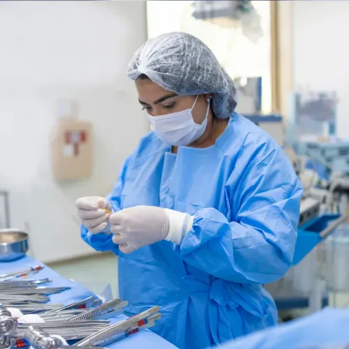 Student in protective gown, mask, and gloves inspects medical instruments in a clinical lab setting.