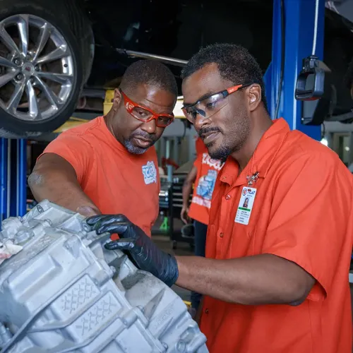 Instructor and student examine a transmission assembly while wearing safety glasses in an automotive lab.