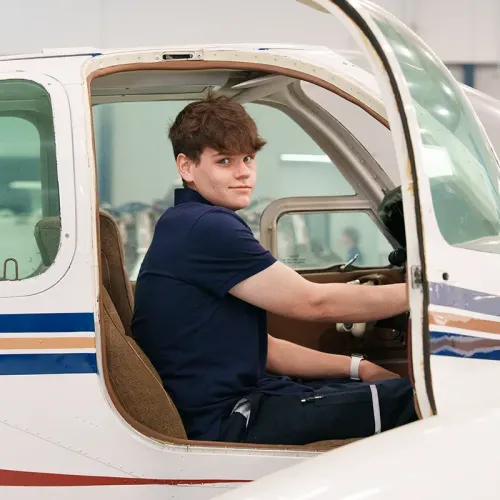 Student seated in a small aircraft cockpit during avionics training in an aviation lab.