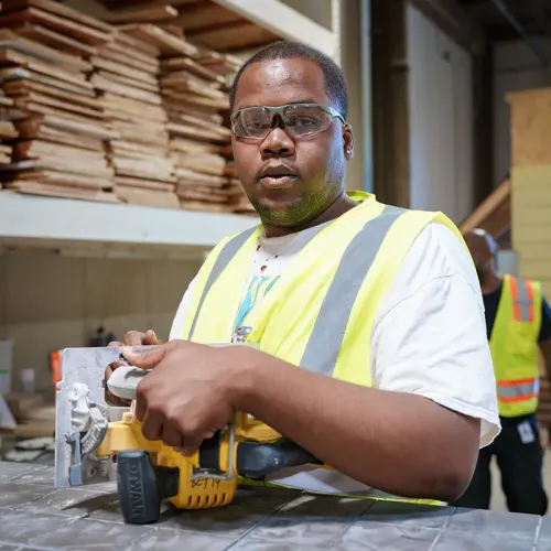 Student wearing safety glasses operates a circular saw on a workbench in a construction workshop.