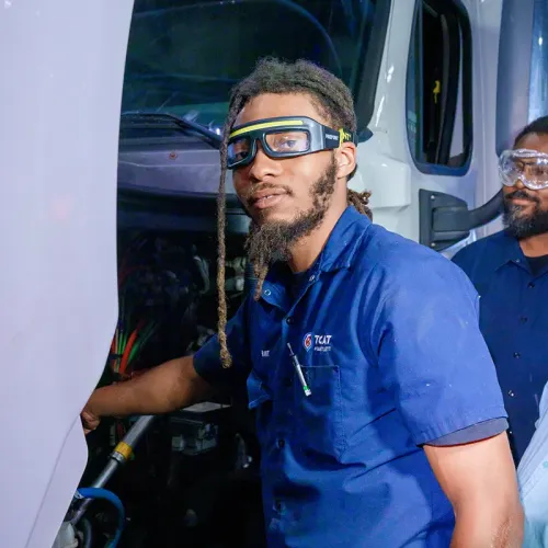 Student wearing safety goggles works on a semi-truck engine in a diesel technology lab.