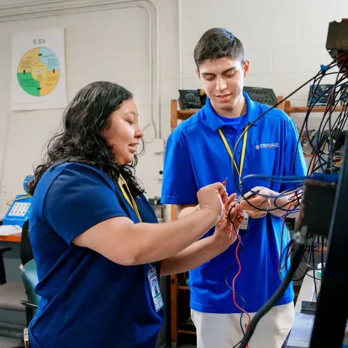 Two students connect wires and work with electronic equipment in an electronics technology lab.