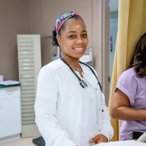Student wearing a stethoscope stands beside a hospital bed in a nursing training lab.