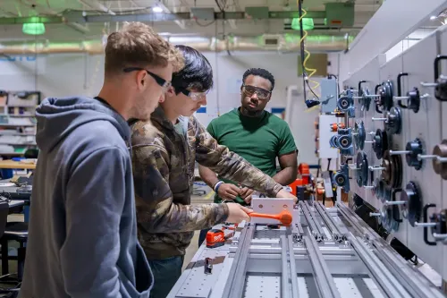 Students wearing safety glasses work with an industrial automation training system in a manufacturing lab.