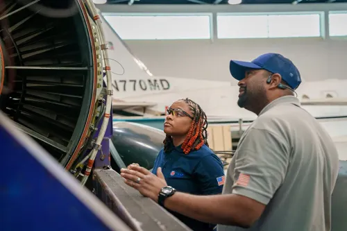Instructor and student inspect a jet engine in an aircraft maintenance training hangar.