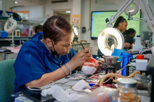 Student uses hand tools to shape a dental model at a workstation in a dental lab.