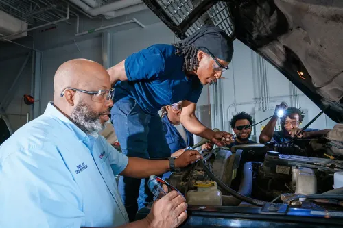 Instructor and students examine an engine compartment during hands-on diesel equipment training.