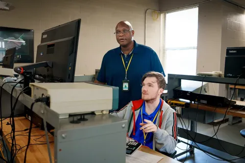 Instructor and student review information on a computer monitor in an electronics technology classroom.