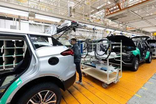 Worker assembling electric SUVs on a factory production line beside carts of vehicle components.